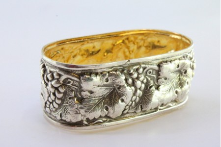 Argola de guardanapo em prata em forma oval com relevos de folhas e uvas.